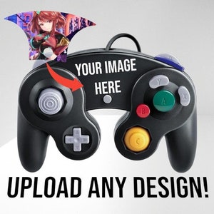 May include: A black GameCube controller with a customizable faceplate. The faceplate has the text "YOUR IMAGE HERE" printed on it. The controller has a variety of buttons, including A, B, X, Y, and C.