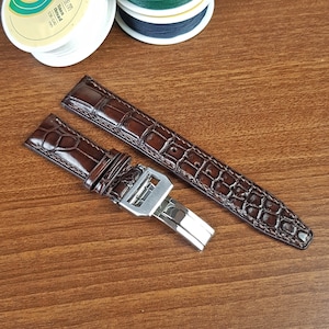 May include: A brown leather watch strap with a crocodile pattern and a silver buckle.