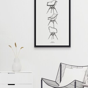 May include: A black and white line drawing of a chair, repeated three times in a vertical stack. The drawing is framed in a black frame and hung on a white wall. The text "Eames Chair" is printed below the drawing.