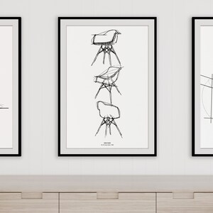 May include: Three black framed prints on a white wall above a light wood cabinet. The center print features a black and white line drawing of a chair in three different positions. The text "Eames Chair" is below the drawing. The left print features a black and white line drawing of a building. The right print features a black and white line drawing of a building with the text "Guggenheim Tower, London" below the drawing.