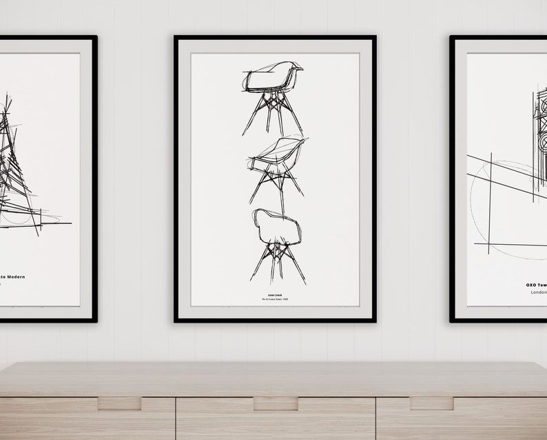 May include: Three black framed prints on a white wall above a light wood cabinet. The center print features a black and white line drawing of a chair in three different positions. The text "Eames Chair" is below the drawing. The left print features a black and white line drawing of a building. The right print features a black and white line drawing of a building with the text "Guggenheim Tower, London" below the drawing.