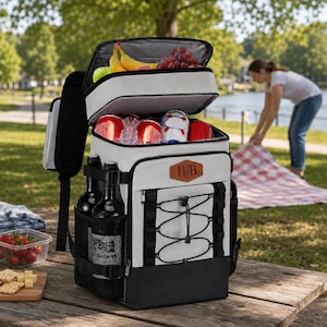 Puede incluir: Una mochila térmica gris claro y negra con un compartimento superior que contiene plátanos y uvas. La sección principal alberga latas de bebida rojas y hielo. Un parche de cuero marrón con las letras HB se encuentra en la parte frontal, que cuenta con cordones elásticos negros y bolsillos laterales de malla.