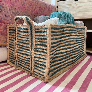 May include: A rectangular jute storage basket with a striped design in natural and teal green. The basket has sturdy handles and is filled with folded textiles. The basket sits on a pink and white striped rug.