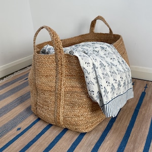 May include: A large, natural jute storage basket with two handles. The basket is filled with a white and blue patterned fabric.