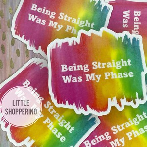 May include: Four rainbow-colored stickers with the text "Being Straight Was My Phase" in white lettering. The stickers are on a gold glitter background.