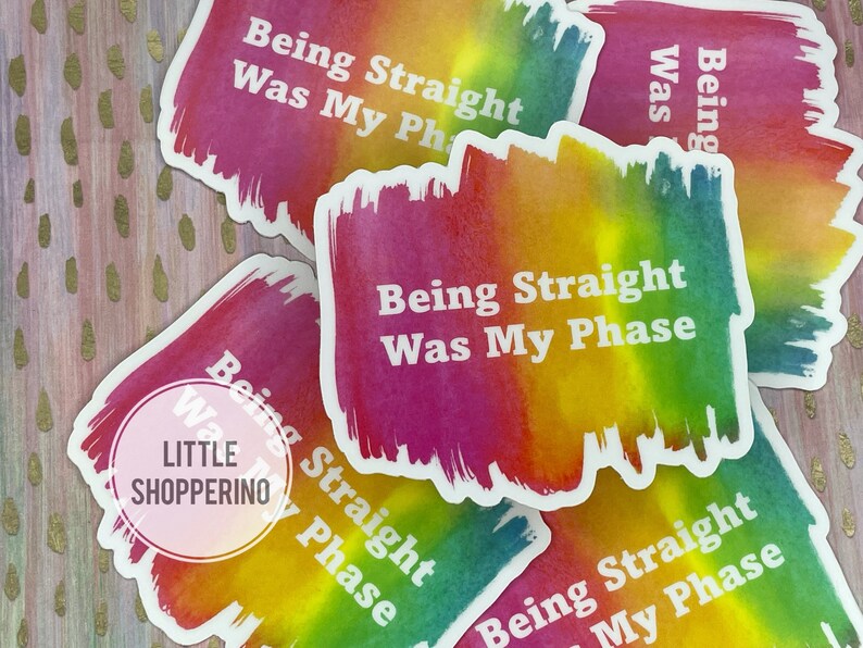 May include: Four rainbow-colored stickers with the text "Being Straight Was My Phase" in white lettering. The stickers are on a gold glitter background.