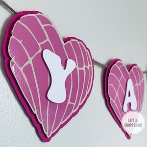 May include: Pink and white heart-shaped banner with the word "MAY" spelled out in white letters. The hearts have a textured pattern.