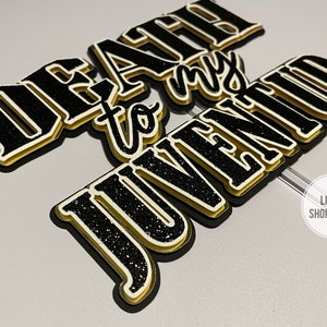 Może przedstawiać: Czarny i złoty topper na tort z tekstem "Death to my Juvenitude".