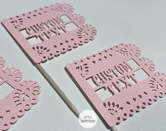 May include: Pink paper cut-out flags on wooden sticks. Each flag has a decorative border and the words "CUSTOM TEXT" cut out. The flags are likely for a party or event.