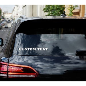 May include: A black car with a white vinyl sticker on the back window that says "CUSTOM TEXT".