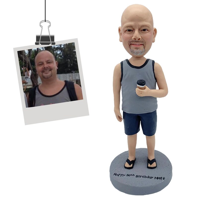 Puede incluir: Figura de bobblehead personalizada de un hombre con camiseta sin mangas gris y pantalones cortos azules, sosteniendo una taza de caf&eacute;. La figura est&aacute; sobre una base gris con la inscripci&oacute;n "Happy 50th Birthday Matt." Una foto est&aacute; sujeta en la parte superior.