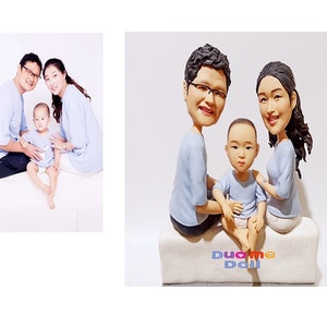 May include: A custom-made figurine of a family of three, a man, a woman, and a child. The figurines are made of clay and are painted in realistic colours. The family are wearing blue shirts and the child is sitting on the lap of the woman. The figurines are sitting on a white base with the words "DuoMe Doll" written on it.