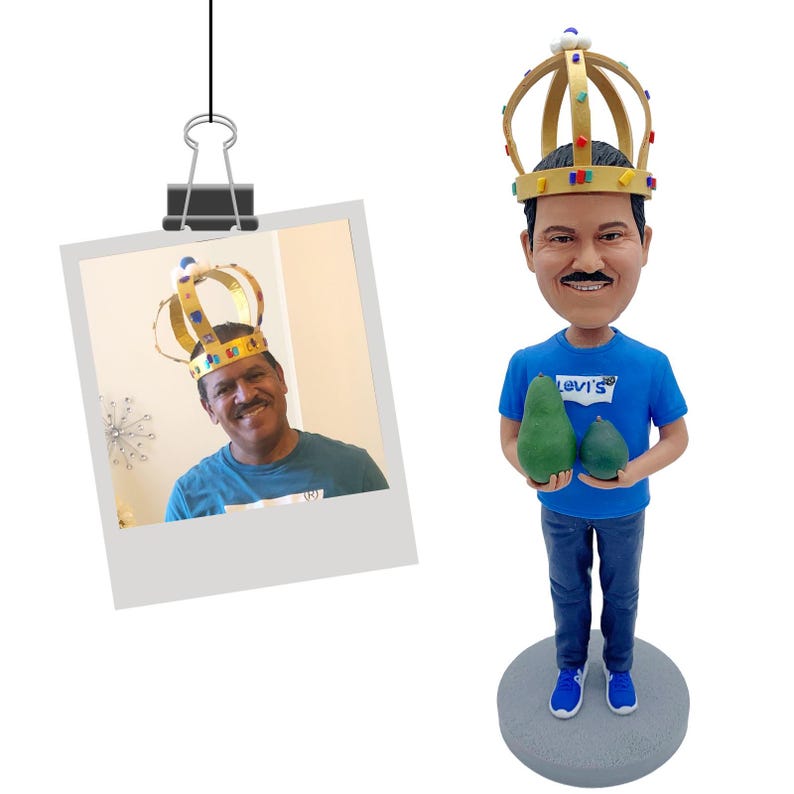 Puede incluir: Una figura de un hombre con una corona dorada y una camiseta azul con el logo de Levi's, sosteniendo dos aguacates verdes. La figura est&aacute; sobre una base gris. Se adjunta una foto de un hombre con una corona.
