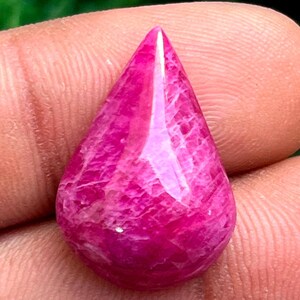 Może przedstawiać: Różowy kamień szlachetny w kształcie łzy, gładki i wypolerowany. Kamień ma intensywny różowy kolor z białymi żyłkami.