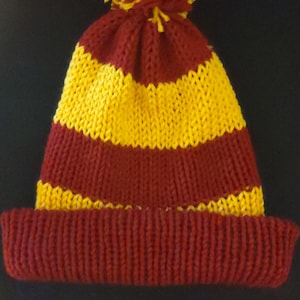 May include: A knitted hat with a red and yellow striped pattern and a yellow pom-pom on top.