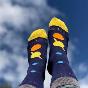 Könnte beinhalten: Ein Paar blaue Socken mit einem Planetenmuster in Gelb, Orange und Blau. Die Socken werden getragen und die Zehen zeigen zum Himmel.