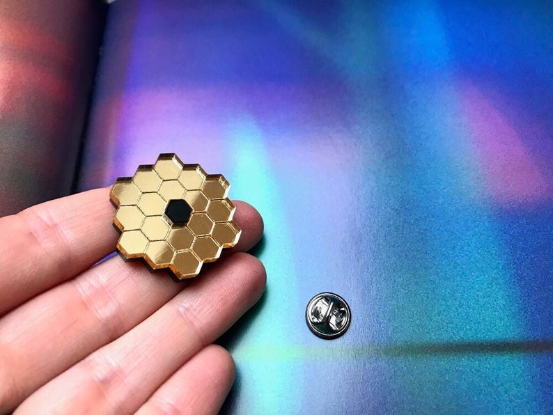 May include: Gold-toned pin with a honeycomb design and a black center. The pin is on a hand.