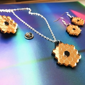 May include: A gold necklace with a hexagonal pendant, a matching pair of earrings, and a gold pin. The pendant and earrings are made of mirrored acrylic and have a black center.