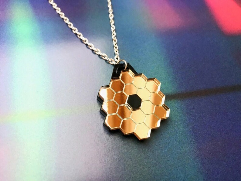May include: A gold and black honeycomb pendant necklace. The pendant is made of mirrored acrylic and has a geometric design.