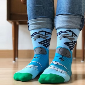 Könnte beinhalten: Ein Paar blaue Socken mit grünem Bündchen. Die Socken zeigen einen grafischen Aufdruck eines Heißluftballons und einer Raumstation.