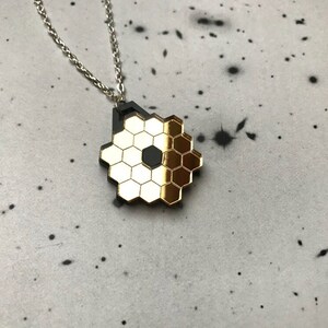 May include: A gold and black honeycomb pendant necklace. The pendant is made of a shiny metal and has a geometric design.