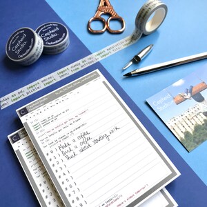 Pu&ograve; includere: Una pila di quaderni a righe grigi e bianchi con un bordo grigio. Il quaderno in cima ha note scritte a mano in inchiostro nero che dicono "Make a coffee", "Drink a coffee", e "Think about starting work". I quaderni hanno il testo "Cepheid Studio" stampato sulla copertina.