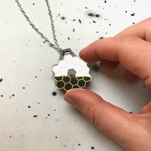 May include: A gold and black geometric pendant necklace with a honeycomb design. The pendant is hanging from a silver chain.