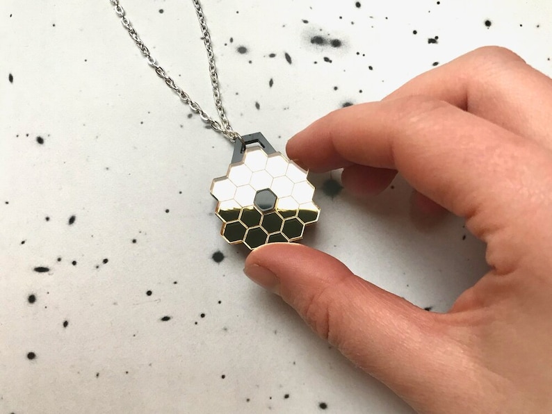May include: A gold and black geometric pendant necklace with a honeycomb design. The pendant is hanging from a silver chain.