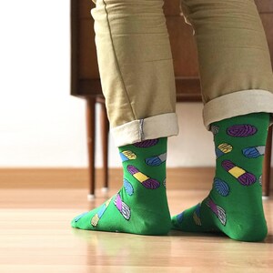 May include: A pair of green socks with a colorful pill pattern. The socks are rolled up at the top and the person is wearing khaki pants.