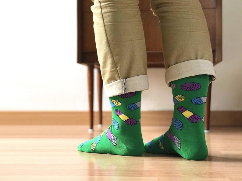May include: A pair of green socks with a colorful pill pattern. The socks are rolled up at the top and the person is wearing khaki pants.