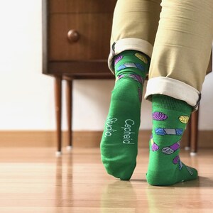 May include: Green socks with a colorful yarn pattern and the text "Cepheid Studio" on the heel.