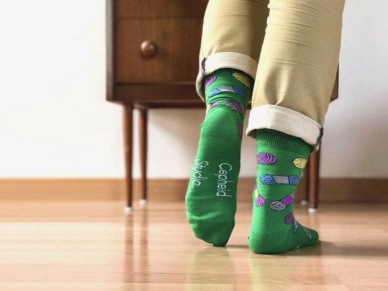 May include: Green socks with a colorful yarn pattern and the text "Cepheid Studio" on the heel.