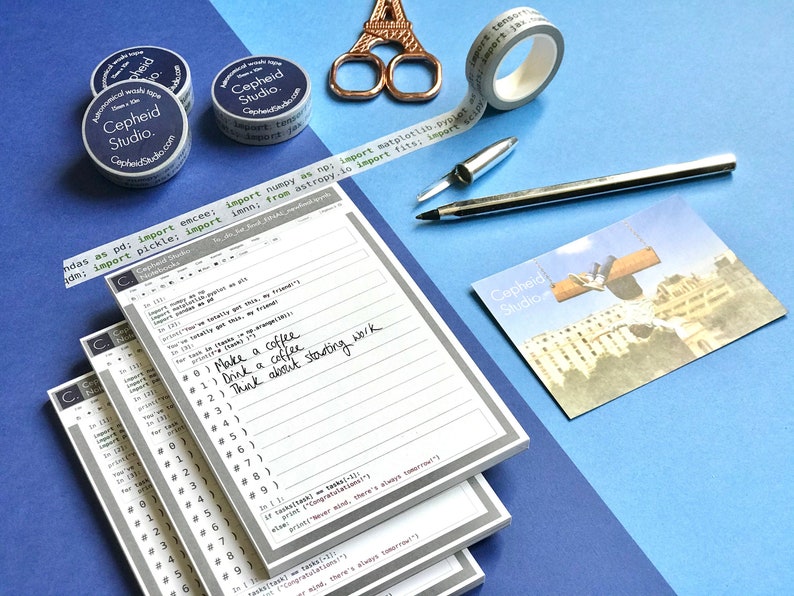 Pu&ograve; includere: Una pila di tre quaderni rigati grigi e bianchi con il testo "Cepheid Studio" stampato sulla copertina. I quaderni sono su una superficie blu con una penna, delle forbici e del nastro washi.