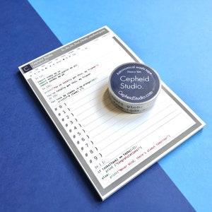 Pu&ograve; includere: Un blocco note grigio e bianco con un frammento di codice in bianco e nero e righe numerate. Un dispenser di nastro washi argentato e blu con il testo "Cepheid Studio" &egrave; sul blocco note. Il nastro washi &egrave; di 15 mm x 10 m.