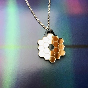 May include: A gold-toned necklace with a hexagonal pendant. The pendant is made of multiple smaller hexagons, creating a honeycomb pattern. The pendant is attached to a silver chain.