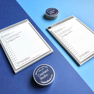 Pu&ograve; includere: Due set di blocchi note bianchi con linee grigie e codice stampato su di essi. I blocchi note sono su una superficie blu. Due rotoli di washi tape sono sulla superficie, uno &egrave; blu e l'altro &egrave; bianco. Il washi tape ha il testo "Astronomical washi tape" e "Cepheid Studio."