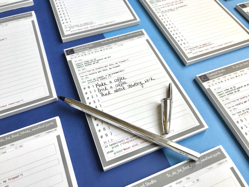 May include: A white notepad with gray lines and a gray border. The notepad has handwritten text that reads "Make a coffee", "Drink a coffee", and "Think about starting work". A silver pen is lying on top of the notepad.