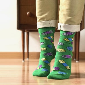 May include: A pair of green socks with a colorful yarn pattern. The socks are worn on a person's feet.