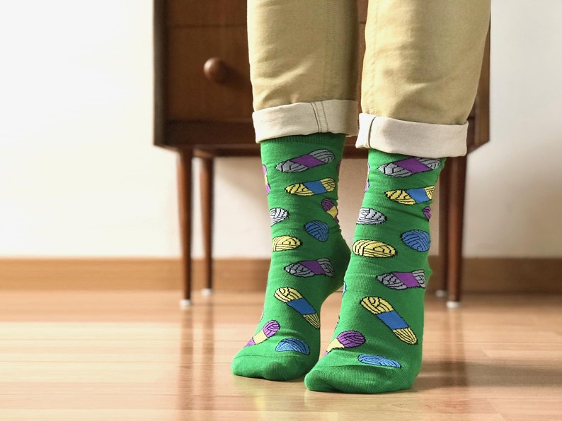 May include: A pair of green socks with a colorful yarn pattern. The socks are worn on a person's feet.