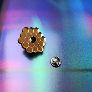 May include: A gold-colored pin with a honeycomb design. The pin is on a iridescent background.