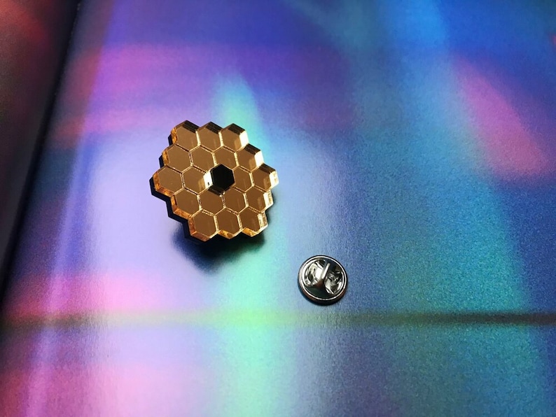 May include: A gold-colored pin with a honeycomb design. The pin is on a iridescent background.