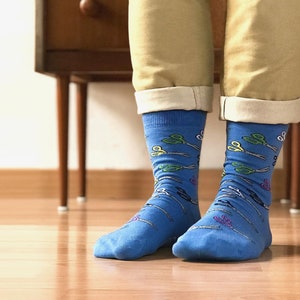 May include: A pair of blue socks with a pattern of colorful scissors. The socks are worn on a person's feet.
