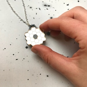 May include: A silver chain necklace with a hexagonal pendant. The pendant is made of black and white metal and has a honeycomb pattern.