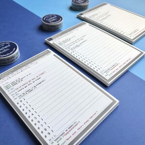 Pu&ograve; includere: Due set di blocchi note bianchi con bordi grigi e pagine a righe. Le pagine dei blocchi note hanno un tema di codice informatico con un design di schermo del computer grigio e bianco. I blocchi note sono su uno sfondo blu e blu chiaro. I blocchi note hanno il testo "Cepheid Studio" stampato su di essi.