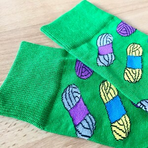 May include: A pair of green socks with a colorful yarn pattern. The socks have a variety of colors including purple, blue, yellow, and gray.