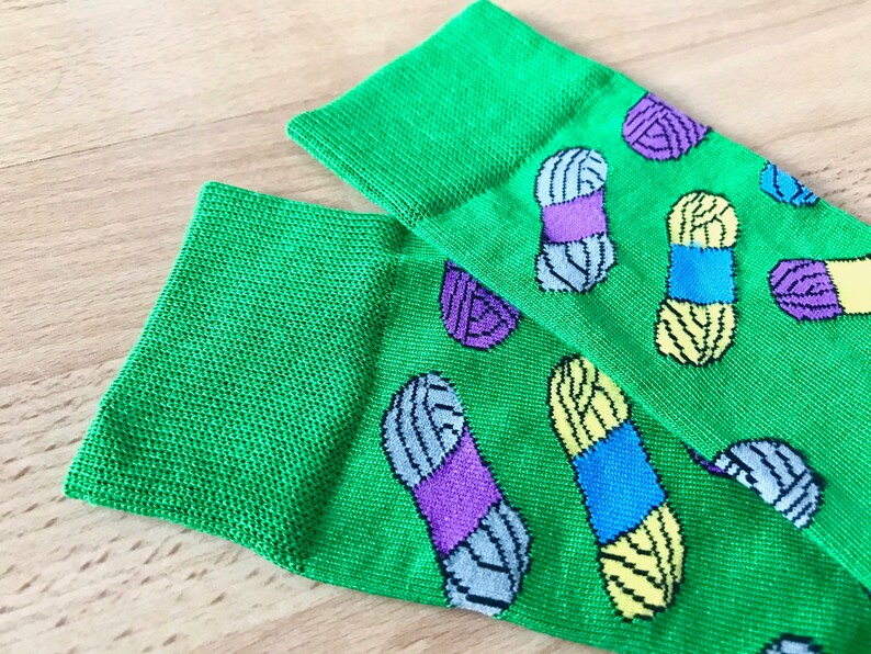May include: A pair of green socks with a colorful yarn pattern. The socks have a variety of colors including purple, blue, yellow, and gray.