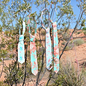 May include: Four patterned neckties hanging on a branch. The ties are made of fabric and have a floral design in shades of blue, pink, and white.