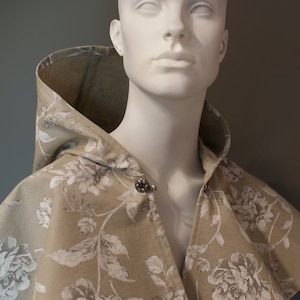 May include: A hooded beige cape with a white floral pattern. The cape has a button closure at the neck.