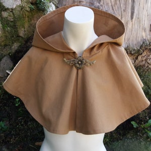 Peut inclure: Une cape à capuche marron avec un fermoir en métal décoratif en forme de fleur. La cape est faite d'un tissu doux et tissé et a un style simple et élégant.
