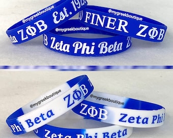 Puede incluir: Una colección de pulseras de silicona azul con texto en blanco. El conjunto superior muestra Zeta Phi Beta, ZΦB Est. 1920 y FINER ZΦB. El conjunto inferior presenta pulseras de silicona azul y blanca con el texto Zeta Phi Beta y ZΦB.